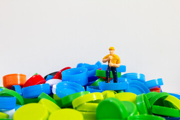 Fototapeta premium small figure worker with pile of many color plastic caps