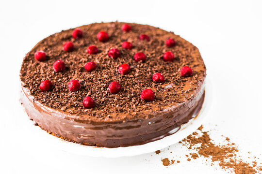 Homemade chocolate cake with cherries in a plate on a white background. Сocoa scattered on a table.