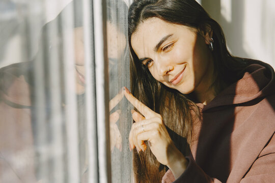 Sunny day. Woman llok at the window. Warm clothes