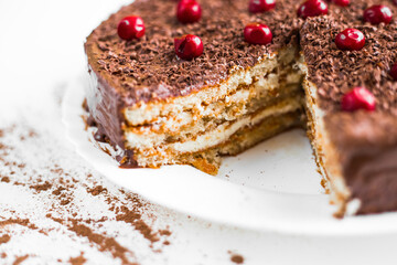 Close-up home chocolate cake with cherries in a plate on a white background. Сocoa scattered on the table. Light rays fall on the table