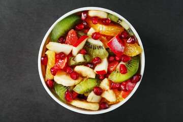 Fruit salad in a white cup on a black background, free space for text.