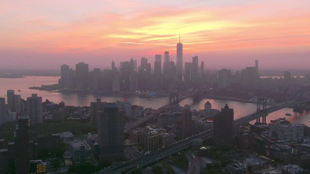 Aerial shot of bridges on East River in city against sky, drone flying forward towards buildings in Manhattan during sunset - New York City, New York