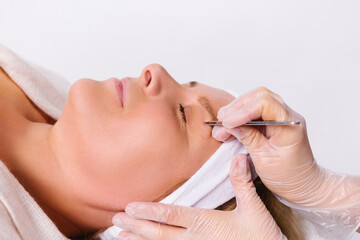 An enlarged photo of a senior woman in the salon. The hands of the beautician pluck the eyebrows. Beauty concept. White background.