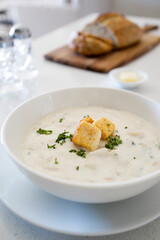 Bowl of Clam Chowder with Whole Grain Bread on a White Kitchen Counter