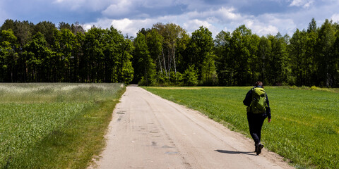 Tourist backpacker walking alone in sunny spring day at countryside. Lubelszczyzna, Poland, Europe.