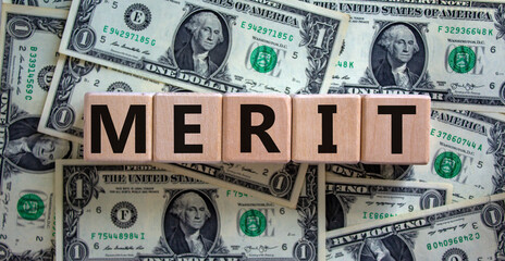 Merit symbol. Wooden cubes with the word 'merit'. Beautiful background from dollar bills, copy space. Business and merit concept.