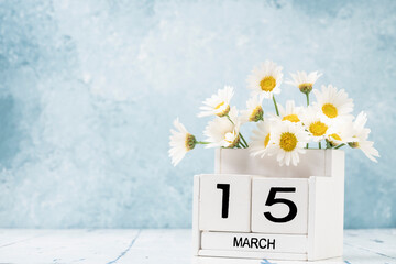 White cube calendar for march decorated with daisy flowers over blue with copy space