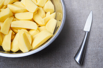 Top view of sliced fresh raw potatoes into pieces in a metal bowl with a knife on burlap cloth. Rustic style, background with ingredient for cooking