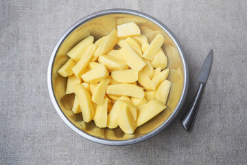 Top view of sliced fresh raw potatoes into pieces in a metal bowl with a knife on burlap cloth. Rustic style, background with ingredient for cooking