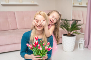 laughing joyful daughter, playfully closes her mother's eyes with her hands, mom holds a bouquet of fresh tulips in her hands. Festive concept mothers day, womens day