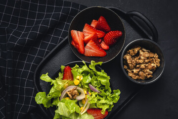 Salad with lettuce, strawberries, red onion, corn; olive oil and walnuts