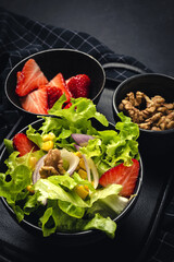 Salad with lettuce, strawberries, red onion, corn; olive oil and walnuts