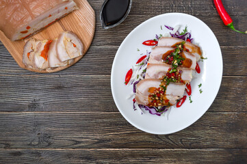 Pork belly with cabbage salad in a white bowl on a wooden background. Chinese cuisine. Top view.