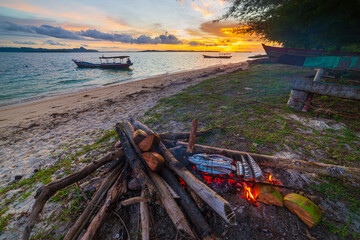 Fish bbq on tropical desert beach. Cooking barbecue with wood fire at sunset, colorful sky on sea, dramatic clouds, getting away, adventure in Indonesia Sumatra Banyak Islands