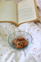 Bowl of chocolate chip cookies and open book on a bed. Selective focus. 