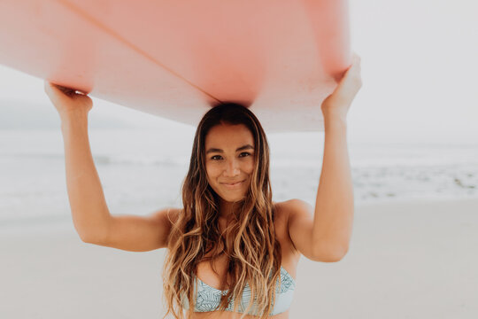Young female surfer carrying surfboard on head at beach, portrait, Ventura, California, USA