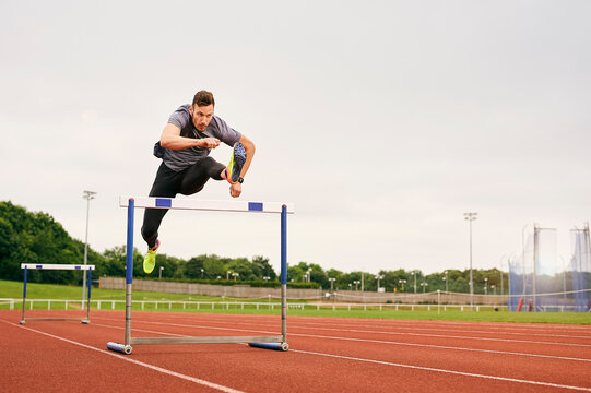 Athlete jumping over hurdle on running track