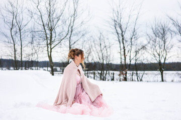Eine wunderschöne sitzt im Schnee im Rosa Tüllkleid sitzt erwartungsvoll und Schauet zur Seite