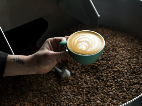 Hand holding cup of coffee over coffee roaster