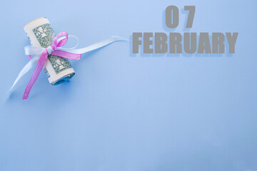calendar date on blue background with rolled up dollar bills pinned by blue and pink ribbon with copy space.  February 7 is the seventh day of the month