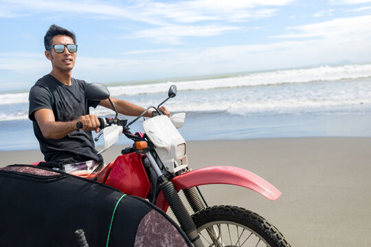 Motorcyclist carrying surfboard on sandy beach, Abulug, Cagayan, Philippines