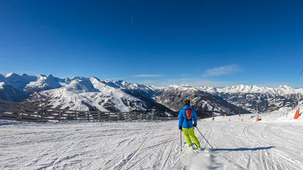 Fotobehang A man in colorful outfit skiing on the slopes of Katschberg in Austria. Panoramic view on the surrounding mountains. Winter wonderland. Sunny winter day. Perfectly groomed slopes. Happiness © Chris