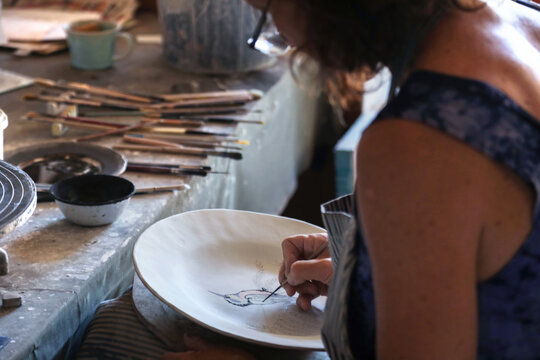 Female potter painting ceramic plate in workshop