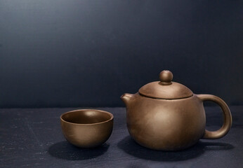 clay brown teapot and teacup on dark background