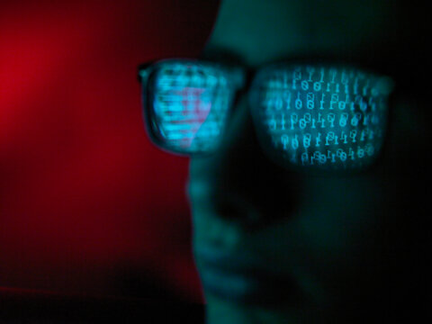 Cyber Crime, reflection in spectacles of virus hacking a computer, close up of face