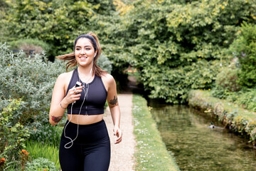 Young female runner listening to earphones while running on riverside path