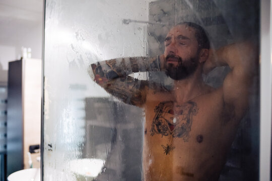 Mid adult man with tattooed chest taking a shower with eyes closed