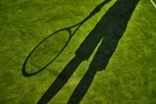 Cropped shadow of tennis player with tennis racket on green lawn