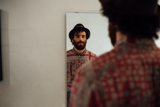 Bearded young man looking into mirror at home