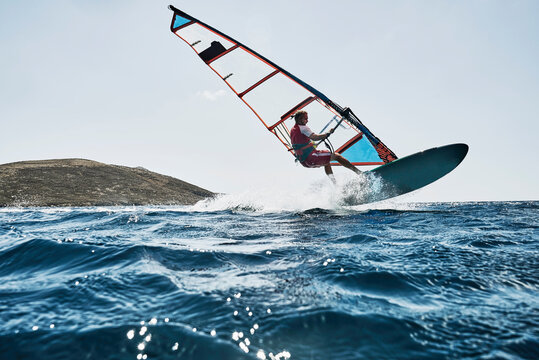Young man mid air while windsurfing ocean waves, Limnos, Khios, Greece