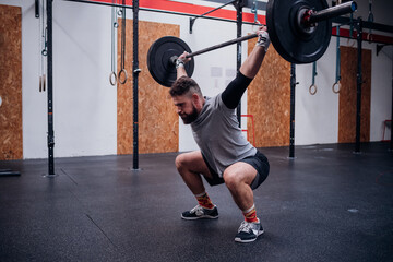 Young man squatting and lifting barbell in gym