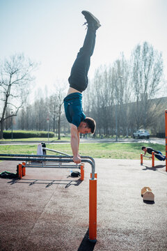 Calisthenics at outdoor gym, young man doing handstand on parallel bars