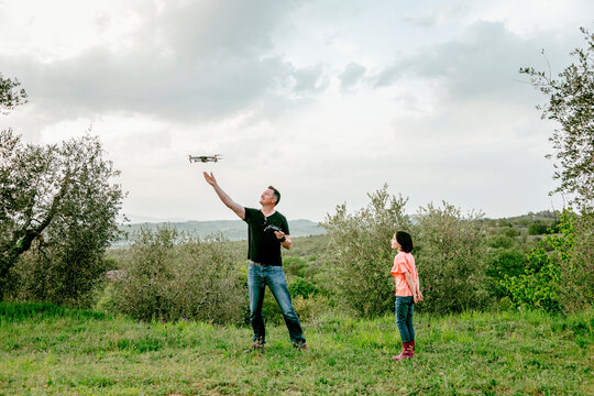Girl watching father flying drone  in scenic field landscape, Citta della Pieve, Umbria, Italy