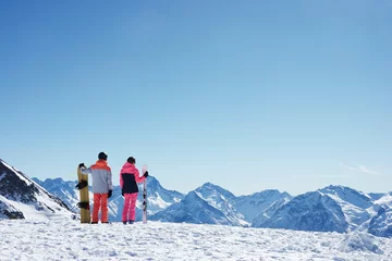  Teenage boy snowboarder with sister skier looking out from snow covered mountain top, rear view,  Alpe-d'Huez, Rhone-Alpes, France © Image Source