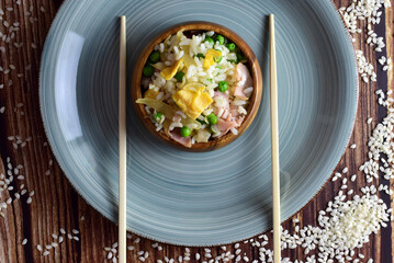 
Three delights rice, in a wooden bowl, accompanied by long chopsticks.