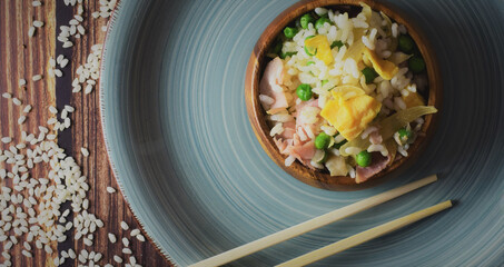 Rice three delights, in a wooden bowl, accompanied by long chopsticks. Zenith view.