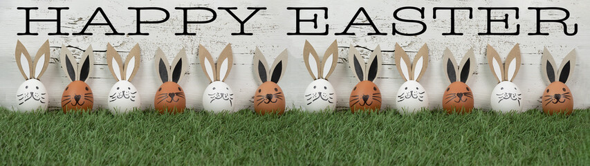 Happy Easter background banner panorama greeting card - Brown and white Easter eggs with bunny ears / Easter bunnies on fresh green meadow, isolated on white vintage shabby wall texture