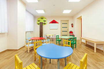 Colorful tables for classes for children and light beige colored game room in the kindergarten.