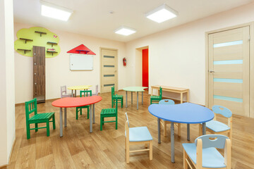 Colorful tables for classes for children and light beige colored game room in the kindergarten.