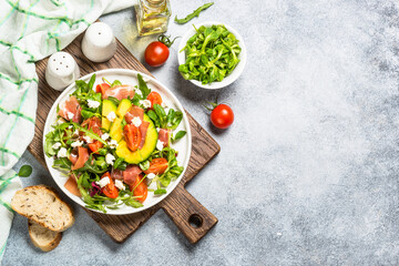 Green salad with avocado, salad leaves, jamon serrano and tomatoes. Healthy diet lunch. Top view at light stone table.