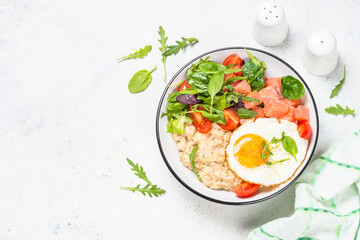 Savory breakfast. Oatmeal porrige with salted salmon, egg and fresh salad. Top view on white table with copy space.