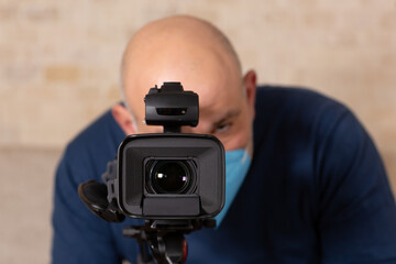 Man wearing face mask, looking to view finder of the camera and filming.