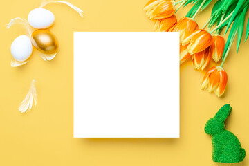 Easter tulips. Golden, white colour egg in basket with spring tulips, feathers on pastel yellow background in Happy Easter decoration. Traditional design in top view.