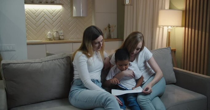 Mother and aunt Europeans help their little African American son draw. International family. High quality 4k footage