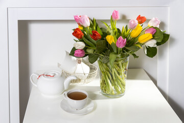 A bouquet of multi-colored tulips in a transparent vase and cup of tea