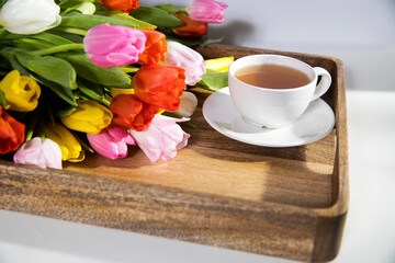 Fototapeta na wymiar A bouquet of multicolored tulips and a cup of tea are on a tray on the table